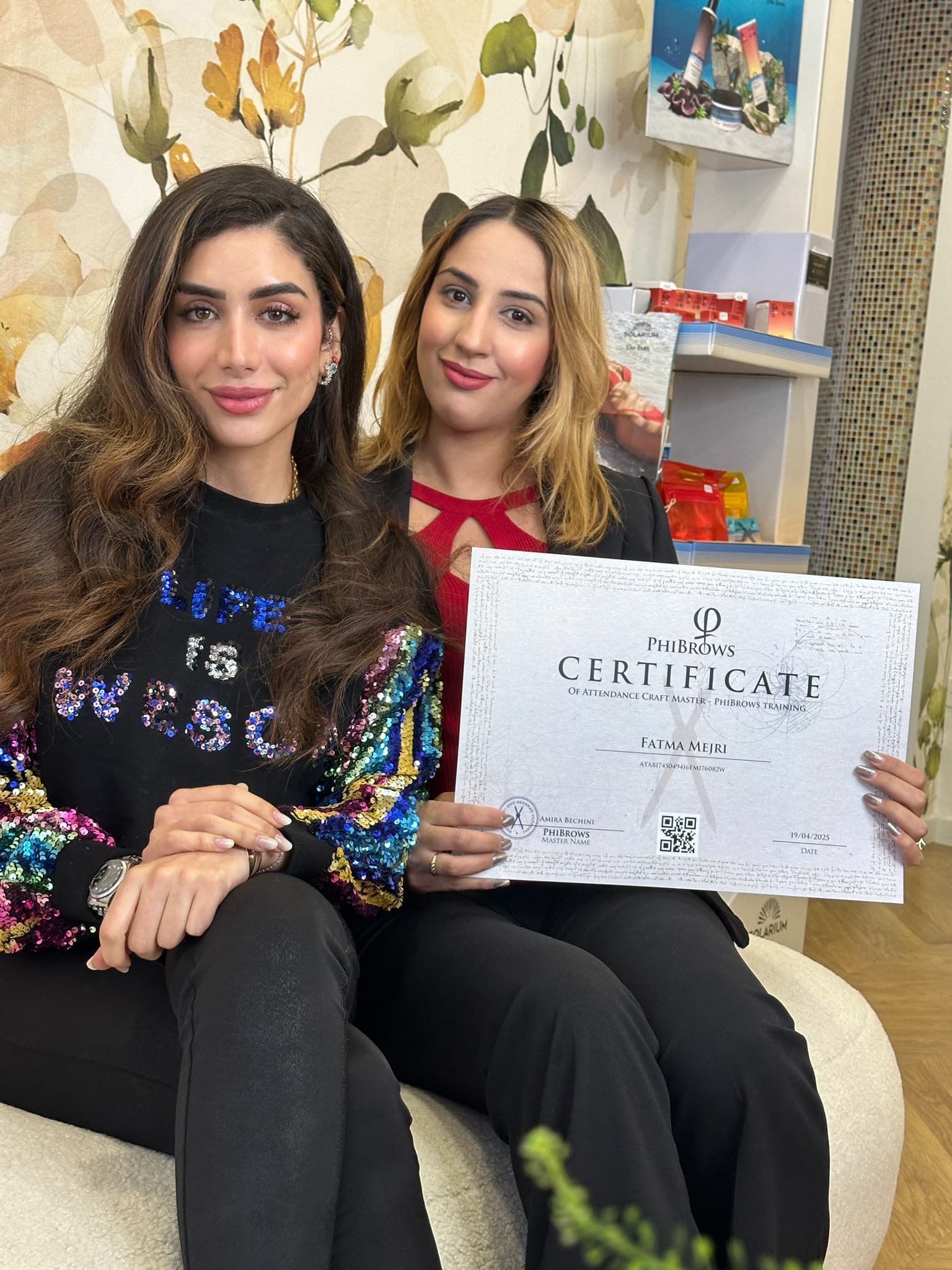 Amira Bechini seated beside a student holding up her PhiBrows certificate.